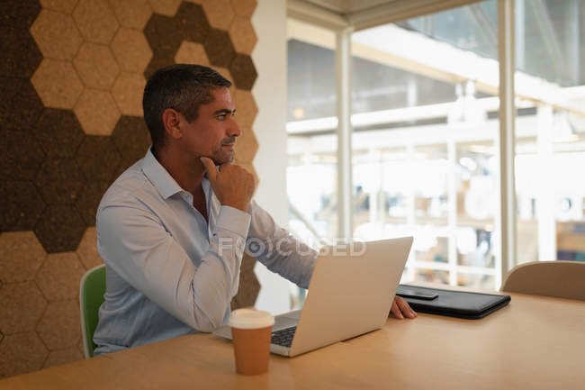 Vista laterale di un uomo d'affari premuroso seduto di fronte al suo computer portatile e guardando lontano in ufficio — Foto stock