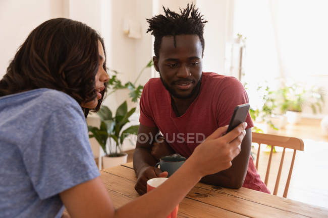 Side view of multi ethnic Couple using mobile phone at home while sitting on chair — Stock Photo