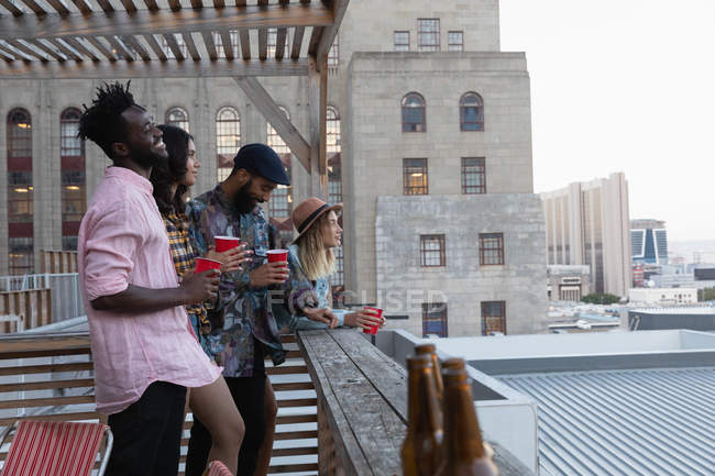 Side view of diverse friends interacting while having cold drink in balcony at home — Stock Photo
