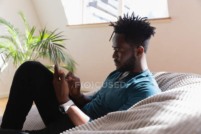 Side view of African-american man using digital tablet at home on sofa — Stock Photo