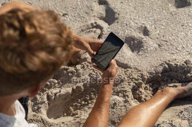 Высокий угол обзора расслабленного человека, пользующегося мобильным телефоном на пляже в солнечный день. Он стоит. — стоковое фото
