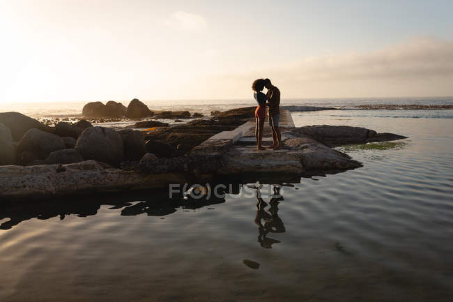 Frontansicht eines afrikanisch-amerikanischen Paares, das in romantischer Stimmung in der Nähe des Meeres auf einem Felsen steht. sie stehen sich von Angesicht zu Angesicht gegenüber und schauen einander an — Stockfoto