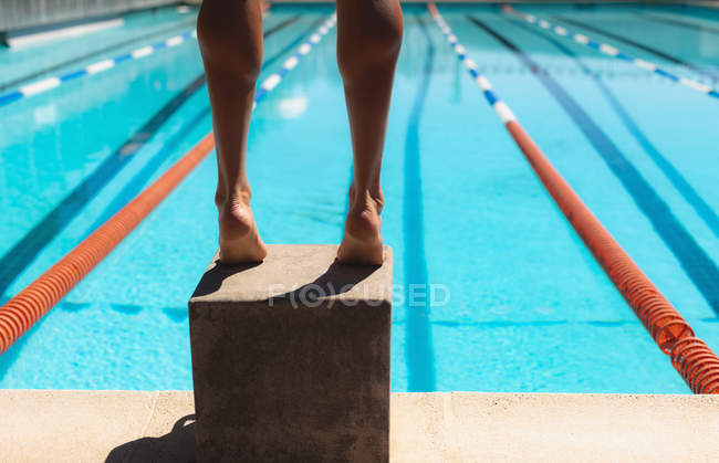 Низька частина чоловічого плавця, що стоїть на стартовому блоці в басейні в сонячний день — стокове фото