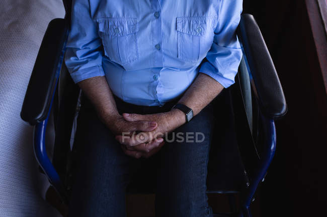 Средний вид на инвалида пожилой женщины со сцепленными руками, сидящей на инвалидном кресле в спальне дома — стоковое фото