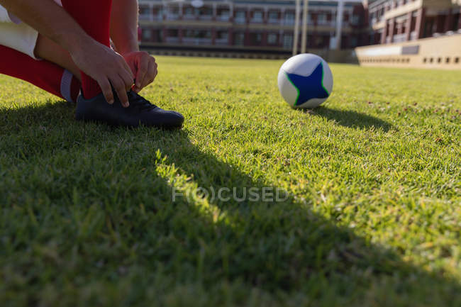 Low section of a male rugby player tying his shoelaces on the rugby ground in the sunshine — Stock Photo