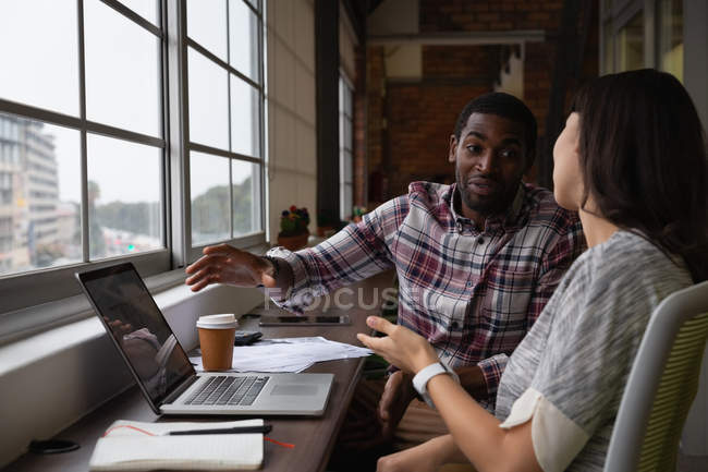 Side view of diverse business people discussing over laptop in office — Stock Photo