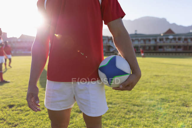 Середина чоловіка регбіст тримає м'яч регбі і стоїть на стадіоні — стокове фото