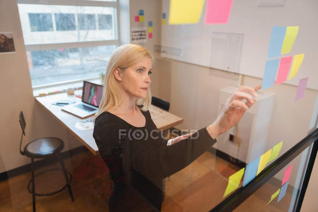 Seitenansicht einer kaukasischen Geschäftsfrau, die auf klebrige Zettel im Büro blickt — Stockfoto