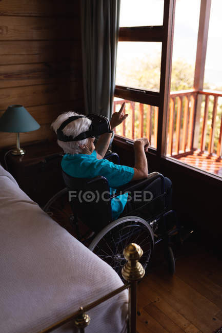 Вид сбоку активной пожилой женщины-инвалида, использующей гарнитуру виртуальной реальности, сидя дома на инвалидной коляске — стоковое фото