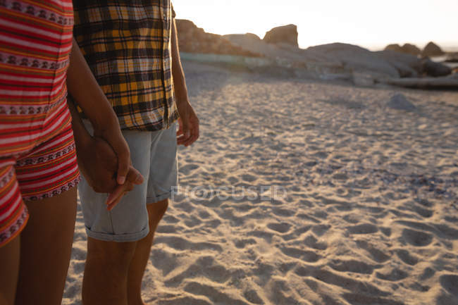 Parte centrale della coppia afro-americana in piedi sulla spiaggia sulla sabbia. Tenendosi per mano l'un l'altro al tramonto — Foto stock