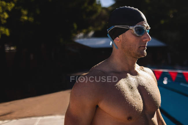 Side view of a Caucasian male swimmer with swim goggle standing near the swimming pool — Stock Photo