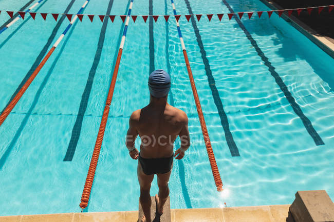 High angle view of young Caucasian male swimmer standing on starting block at swimming pool in the sunshine — Stock Photo