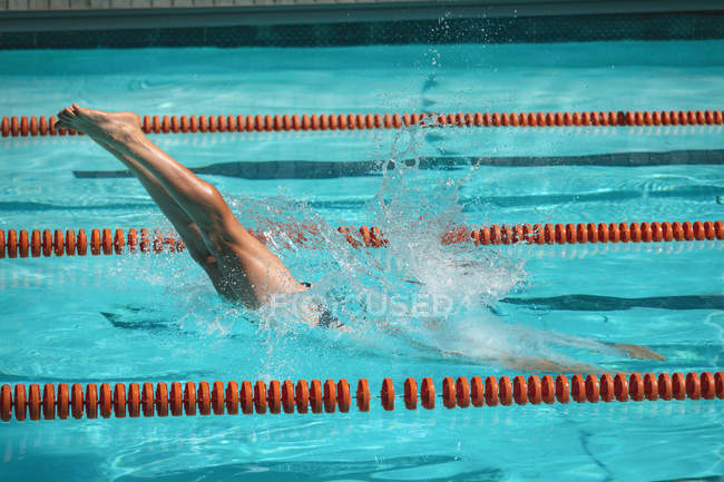 Section basse de jeune nageur mâle plongeant dans l'eau d'une piscine extérieure au soleil — Photo de stock