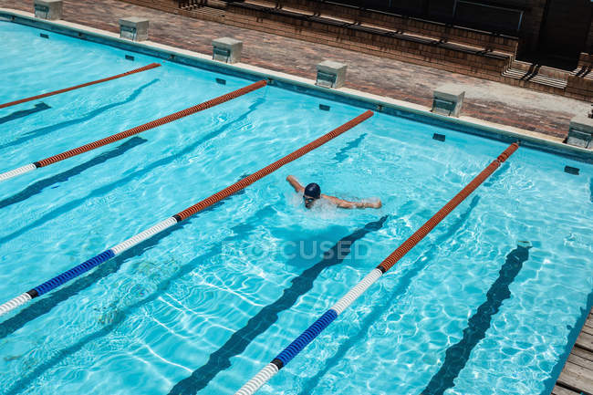Vista de ángulo alto de trabajo duro joven caucásico nadador masculino natación mariposa accidente cerebrovascular en piscina al aire libre en día soleado - foto de stock