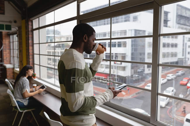 Side view of african american businessman using mobile phone while drinking coffee in office canteen — Stock Photo