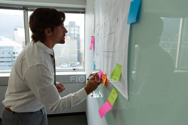 Seitenansicht schöner junger männlicher Führungskräfte, die in einem modernen Büro auf klebrige Notizen schreiben — Stockfoto