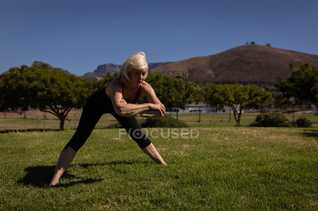 Front view of an active senior woman exercising and stretching in the park on a sunny day — Stock Photo