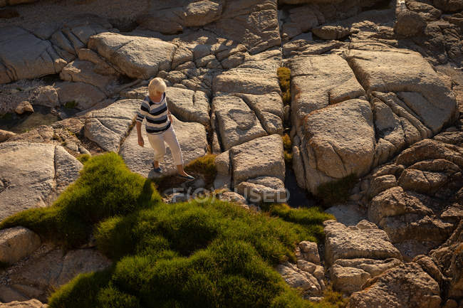 Високий кут зору активної старшої жінки, що йде по скелі на пляжі ввечері — стокове фото