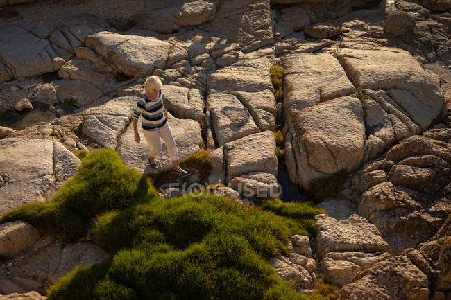 Vista de ángulo alto de una mujer mayor activa caminando sobre la roca en la playa en la noche - foto de stock