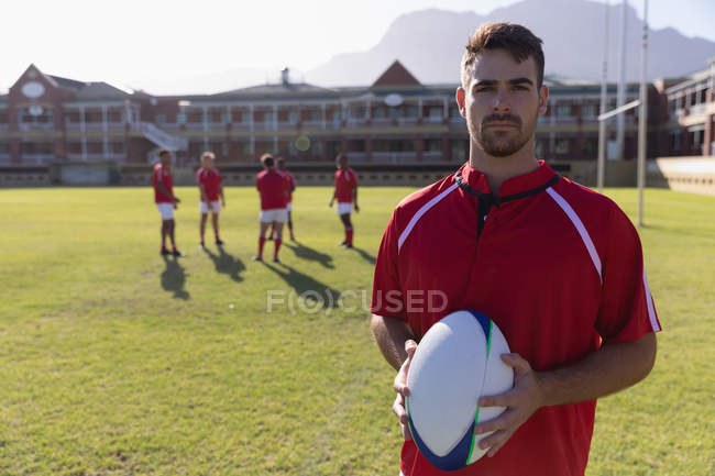Portrait of a male rugby player holding a rugby ball while looking at the camera in the rugby ground — Stock Photo