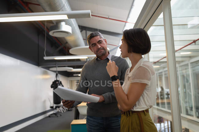 Side view of multi ethnic business people standing in the office and discussing over a blueprint — Stock Photo