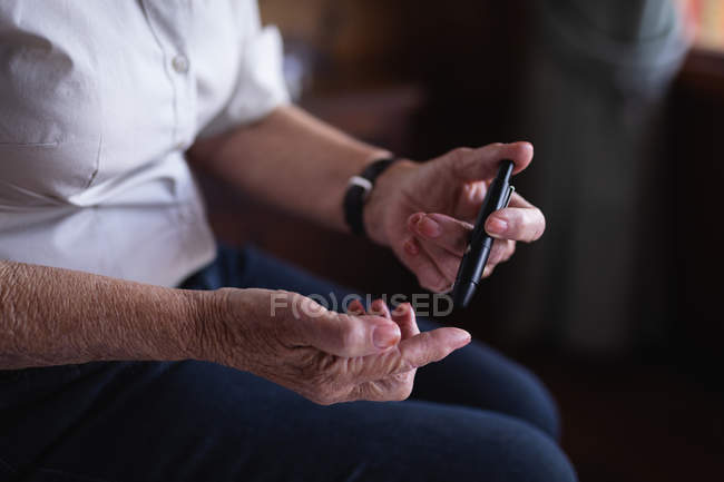 Close-up of an active senior woman checking her blood sugar level with a glucometer on the bed in bedroom at home — Stock Photo