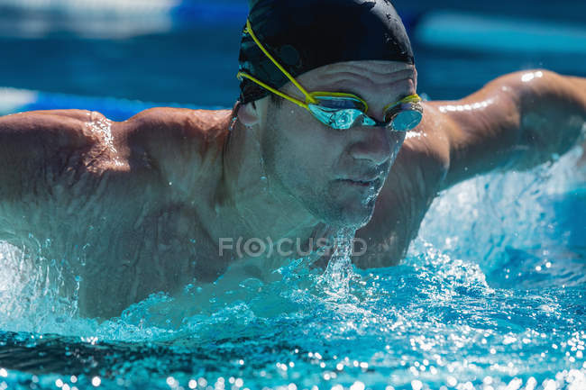 Vue rapprochée d'un nageur mâle nageant en freestyle papillon dans la piscine par une journée ensoleillée — Photo de stock