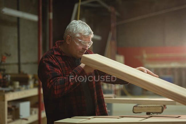 Vista lateral del carpintero tomando medidas de madera en el taller - foto de stock