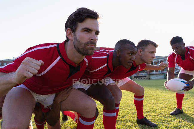 Vista laterale dei giocatori di rugby multietnici maschi che si preparano per una mischia nello stadio in una giornata di sole — Foto stock