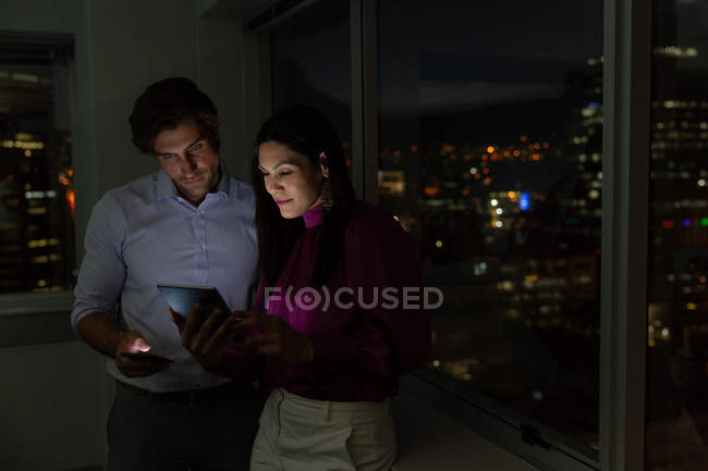 Front view of young multi-ethnic office executives working and discussing over digital tablet near window in a modern office — Stock Photo