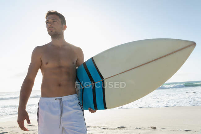 Tiefansicht eines jungen männlichen Surfers mit einem Surfbrett, das an einem sonnigen Tag am Strand steht. Er genießt ihren Urlaub — Stockfoto