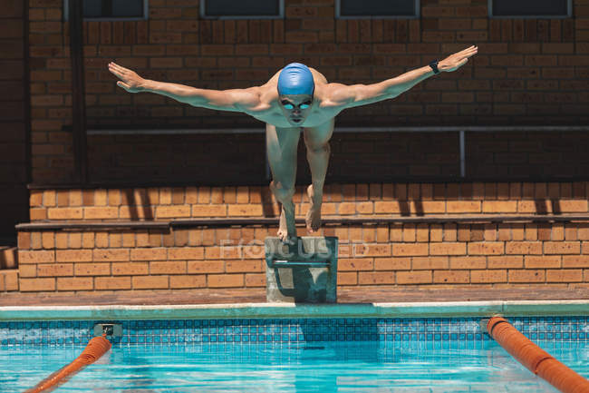 Front view of young Caucasian male swimmer with arms stretched out diving into outdoor swimming pool on sunny day — Stock Photo