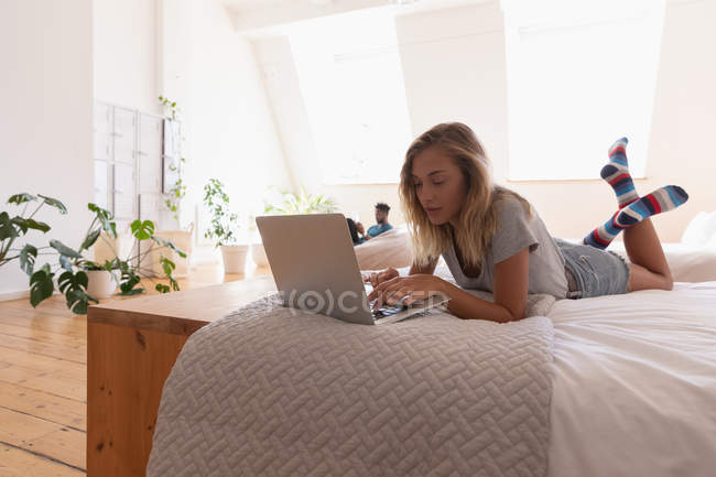 Bella donna che utilizza il computer portatile a casa sdraiato sul letto a casa — Foto stock