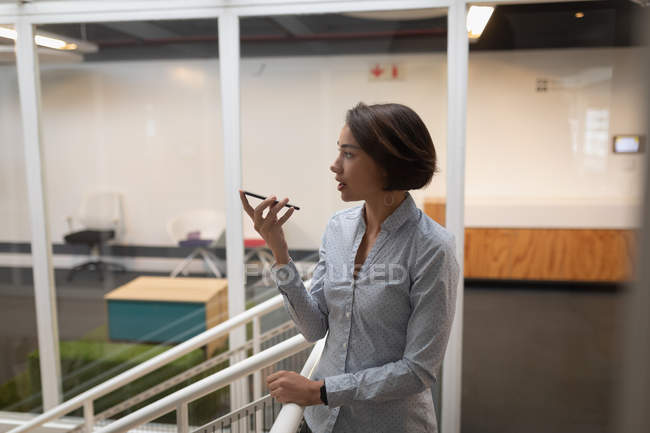 Side view of an Asian businesswoman talking to her mobile phone and leaning on the security barriers in office — Stock Photo
