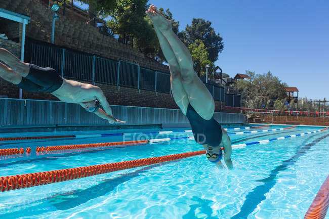 Vue à angle bas des hommes et des femmes nageurs caucasiens sautant dans l'eau en même temps à la piscine au soleil — Photo de stock