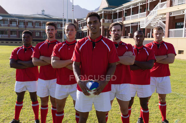 Frontansicht einer Mannschaft männlicher multiethnischer Rugbyspieler, die an einem sonnigen Tag mit einem Rugbyball auf dem Rugbyplatz stehen — Stockfoto
