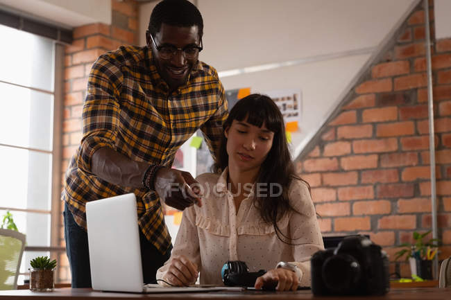 Высокоугольный вид на разнообразных деловых людей, обсуждающих за ноутбуком в офисе. Африканский американец показывает что-то на столе — стоковое фото