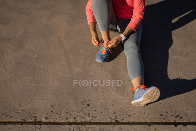 Low section of an active senior woman tying her shoelaces on the beach — Stock Photo