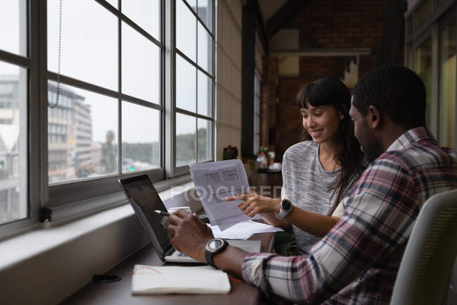 Side view of diverse business people discussing and showing over blueprint in office at desk — Stock Photo
