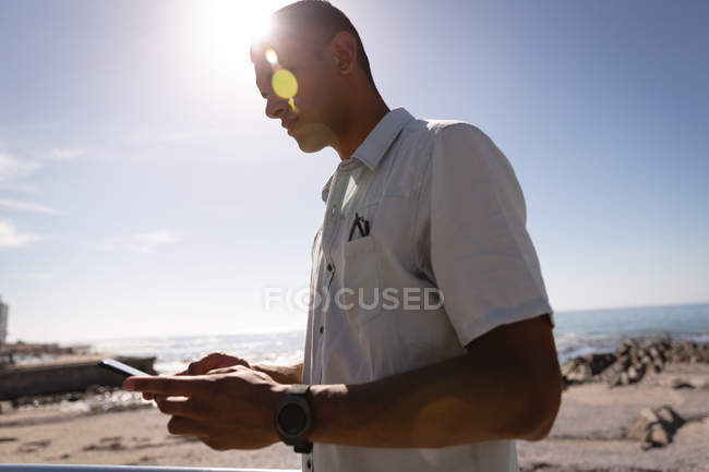 Низький кут зору людини, що використовує мобільний телефон на пляжі в сонячний день — стокове фото