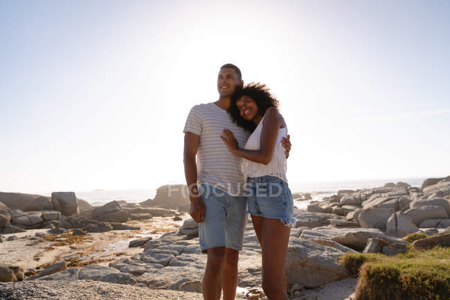 Ángulo de baja vista de pareja afroamericana relajándose y de pie en la roca cerca del lado del mar - foto de stock