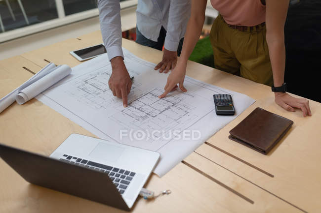 Mittelteil der Geschäftsleute, die im Büro stehen und über einen Bauplan auf dem Schreibtisch diskutieren — Stockfoto