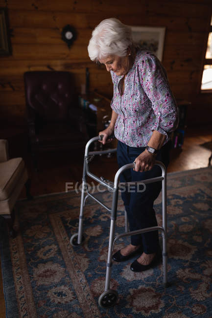 Seitenansicht einer aktiven Seniorin, die mit Rollator im heimischen Wohnzimmer spazieren geht — Stockfoto