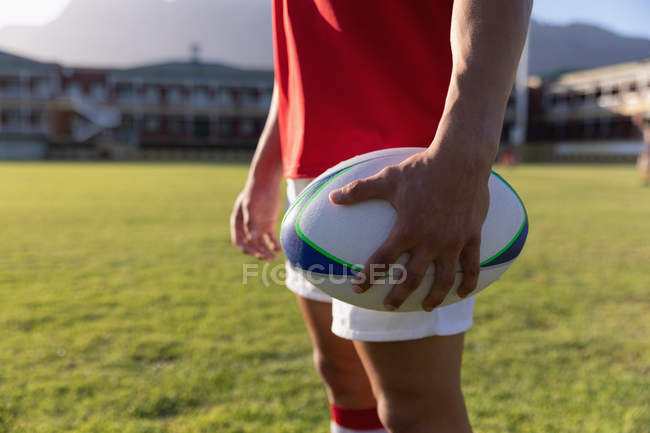 Mittelteil eines männlichen Rugby-Spielers, der einen Rugby-Ball in der Hand hält und im Stadion steht — Stockfoto