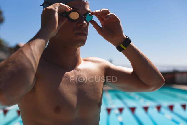Close-up of young Caucasian male swimmer adjusting swimming goggles at outdoor swimming pool on sunny day — Stock Photo