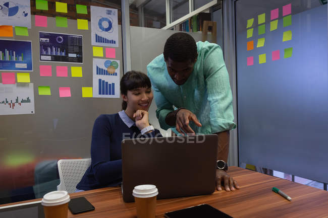 Front view of diverse business people discussing, showing screen over laptop in office at desk — Stock Photo
