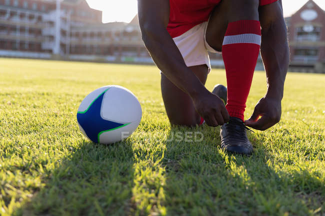 Low section of a male rugby player tying his shoelaces in the stadium — Stock Photo