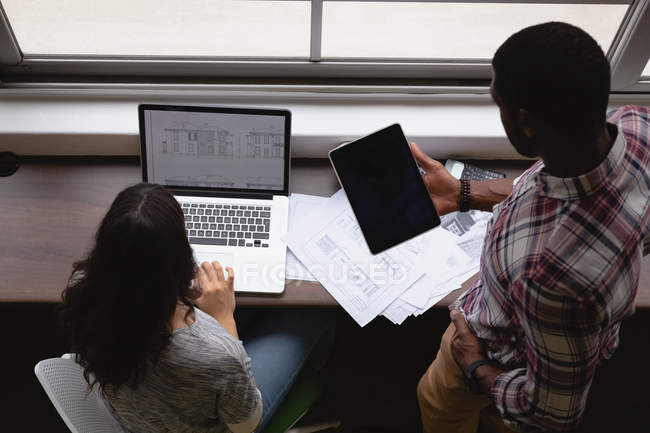 Високий кут зору різних бізнесменів, які працюють над ноутбуком і цифровим планшетом в офісі за столом — стокове фото