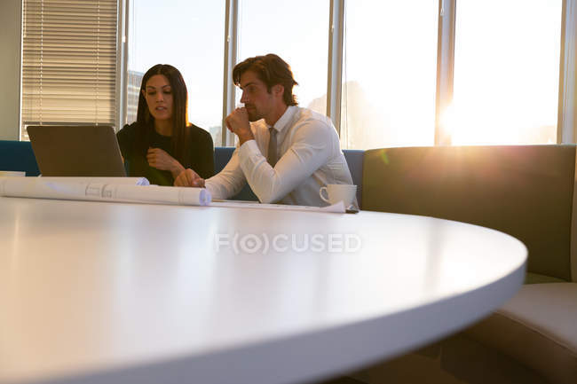 Вид спереду молодих керівників, які сидять за столом і працюють на ноутбуці, насолоджуючись чашкою кави в сучасному офісі — стокове фото