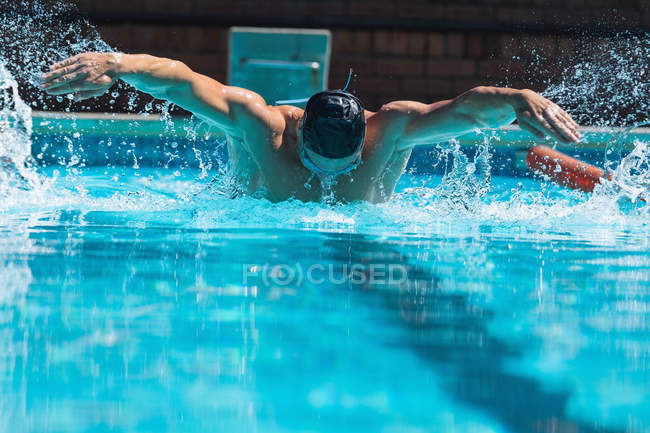 Vista frontal de um nadador masculino com óculos de natação nadando a borboleta na piscina — Fotografia de Stock